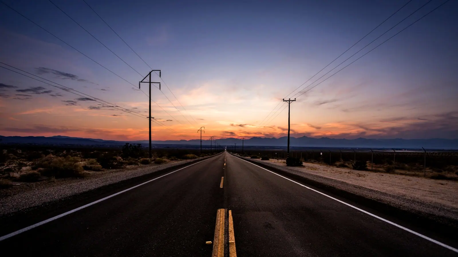 An empty highway stretching toward distant mountains under a golden sunset.