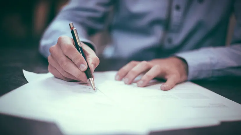 A person signing a printed document at a desk with a pen.