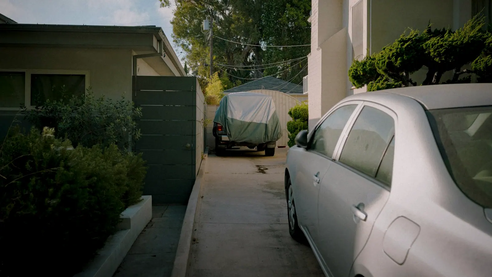 A car parked in a residential driveway beside a house in warm afternoon light.